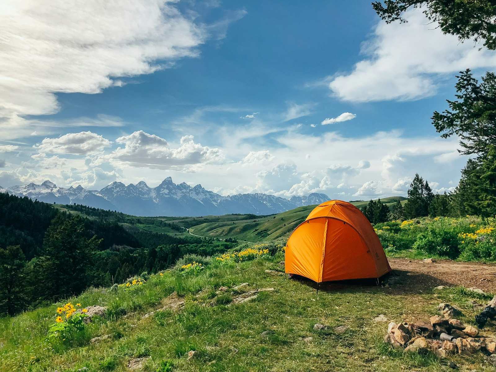 Orange tent on a green hillside with mountain views
