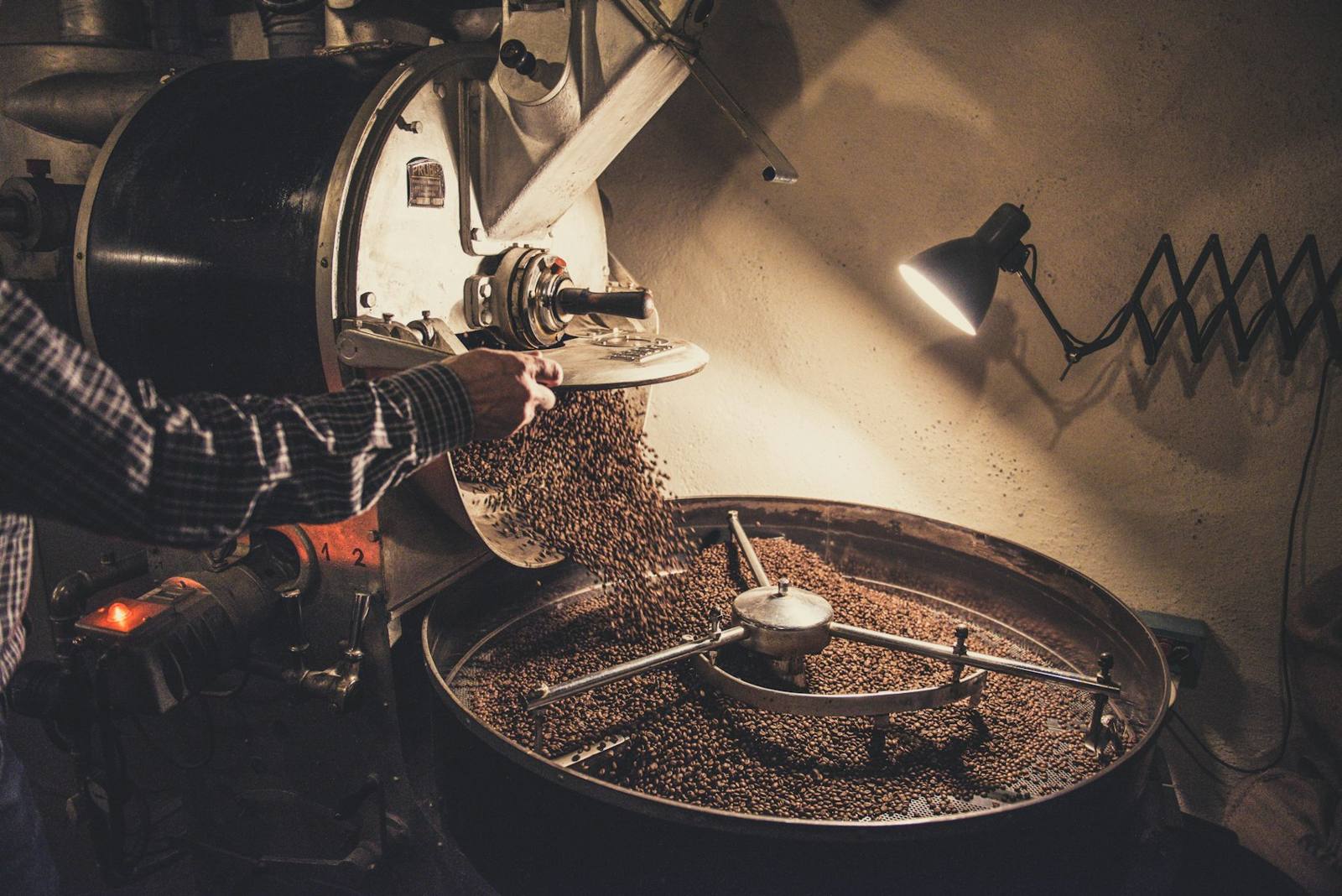 A roaster tending a drum roaster in a dim workshop