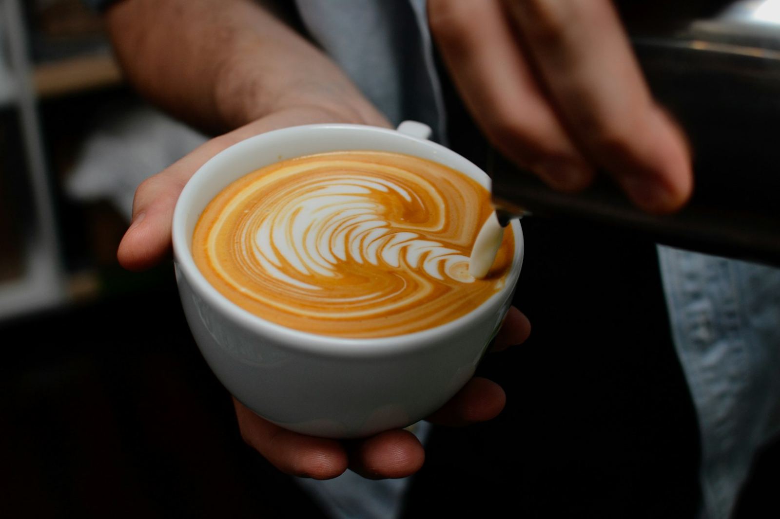 A latte with leaf art held in two hands