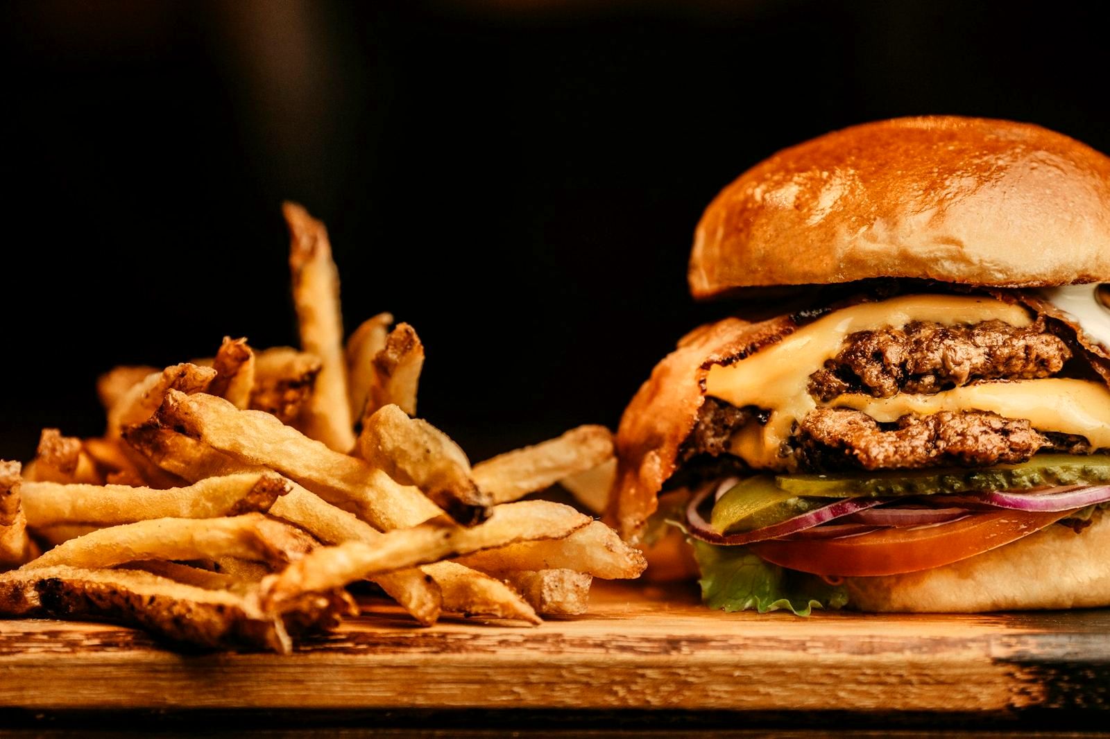A double burger with fries on a wooden board