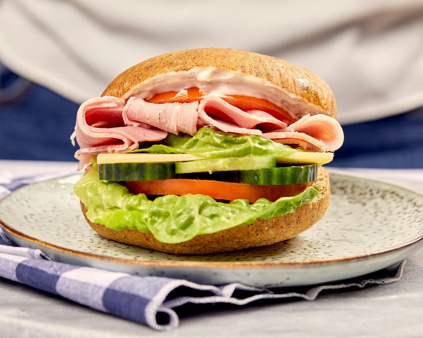 A tall deli sandwich on a bagel with ham, lettuce and tomato