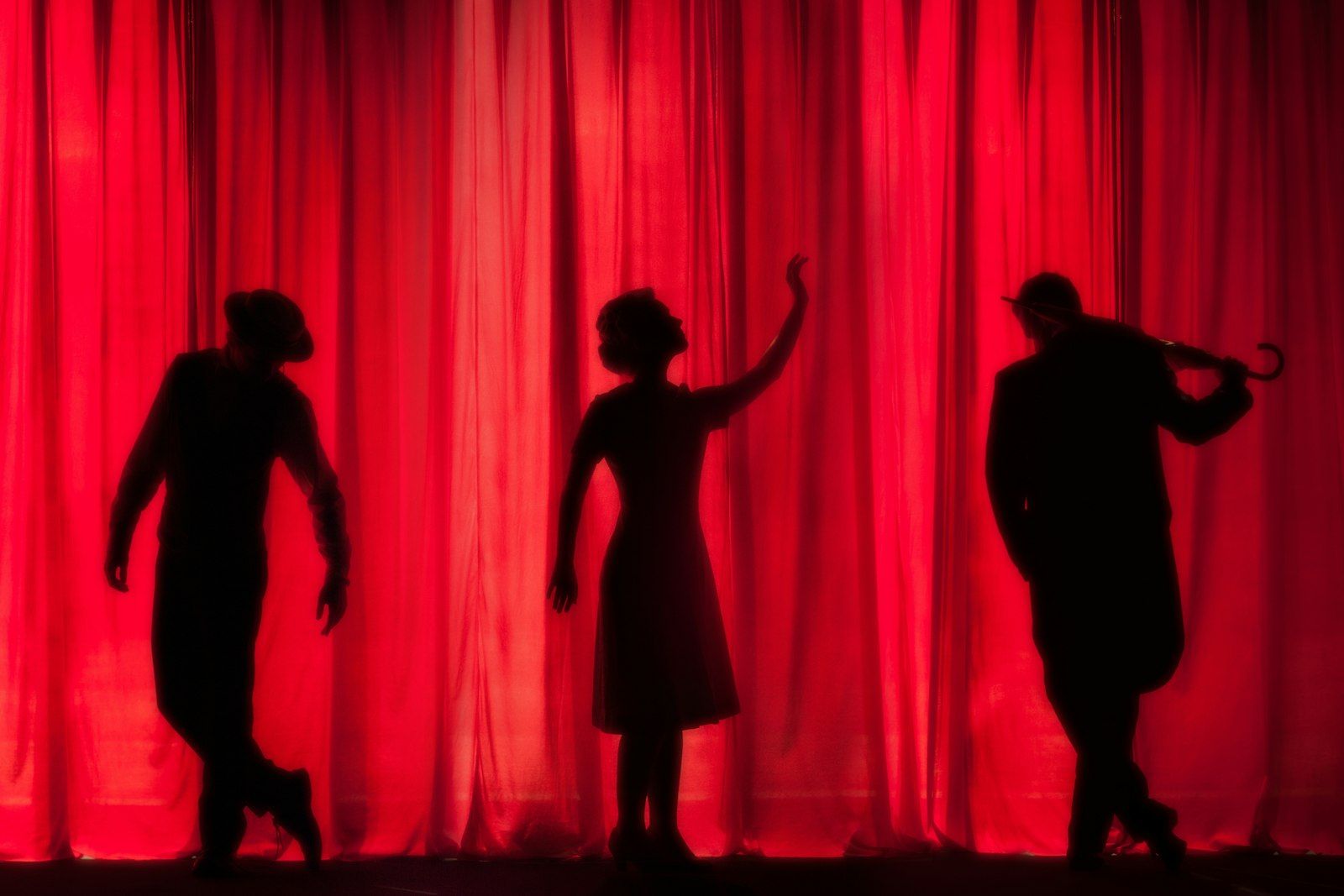 Performer silhouettes against a red curtain