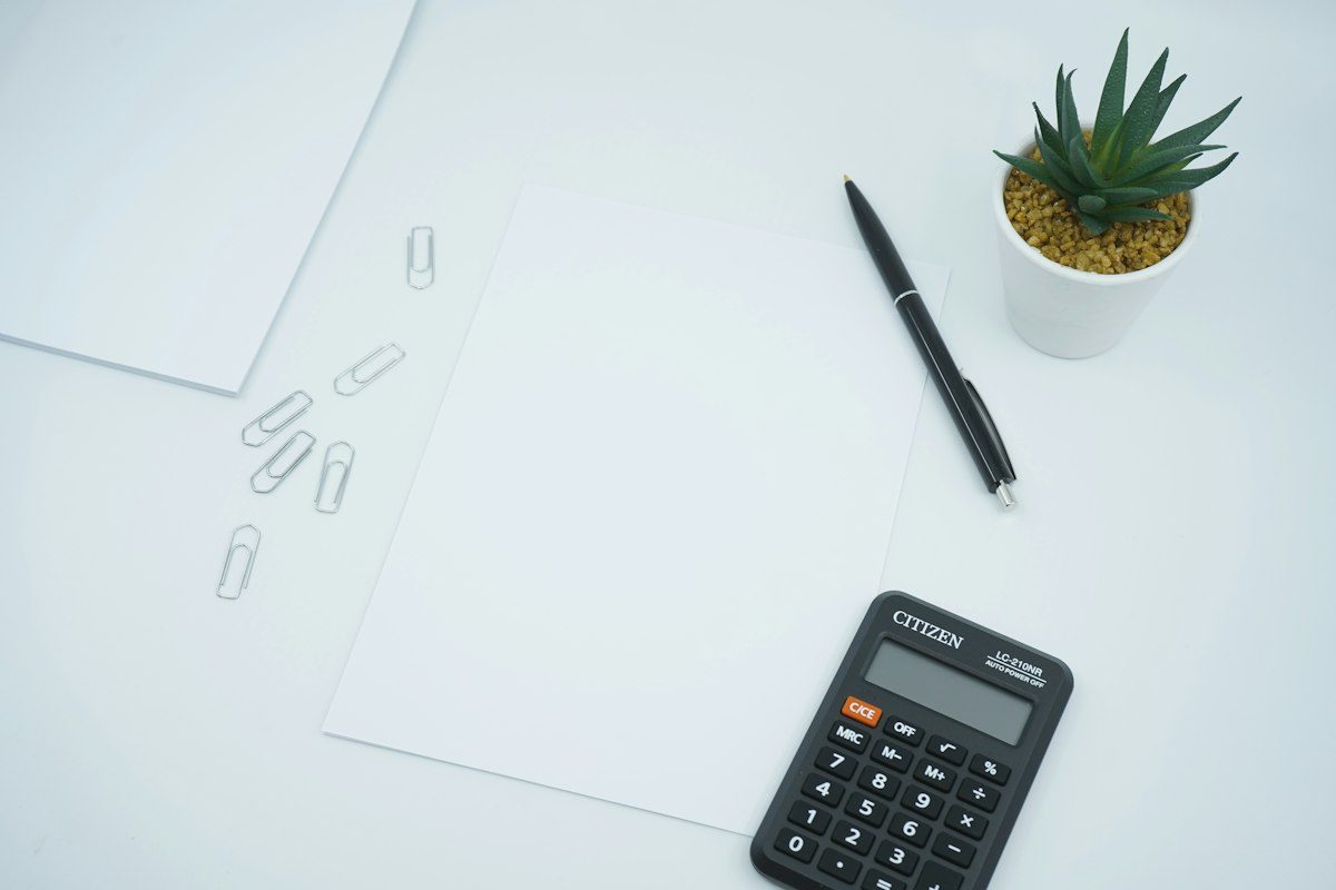 Black calculator beside black pen on white printer paper