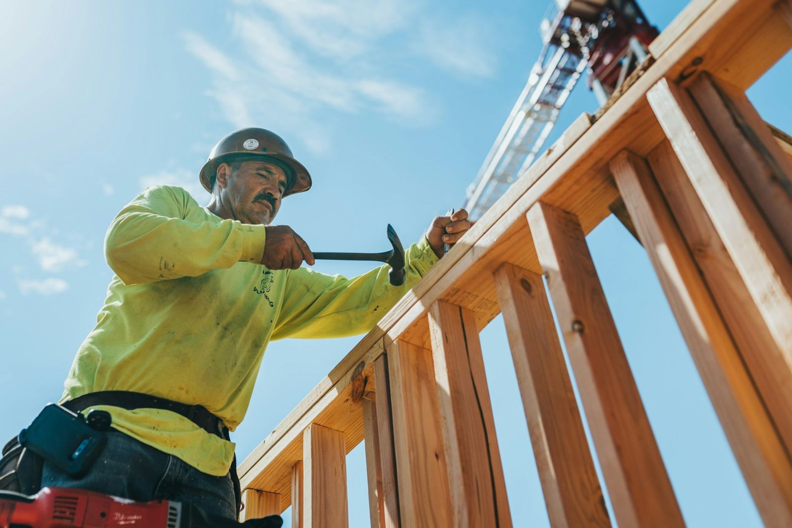 Carpenter nailing wall framing under a blue sky
