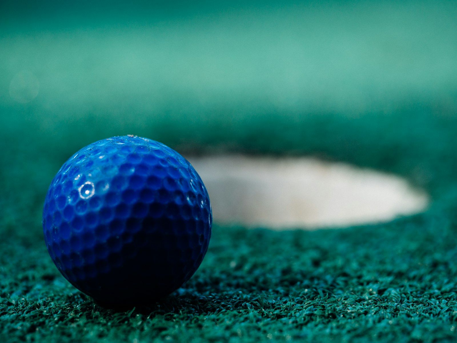Blue golf ball beside the hole