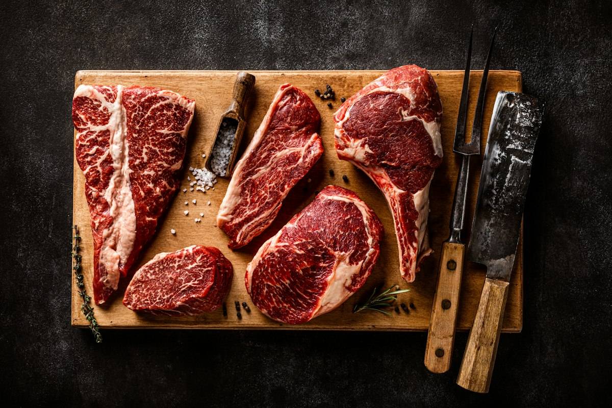 A cutting board with steaks and a knife on it