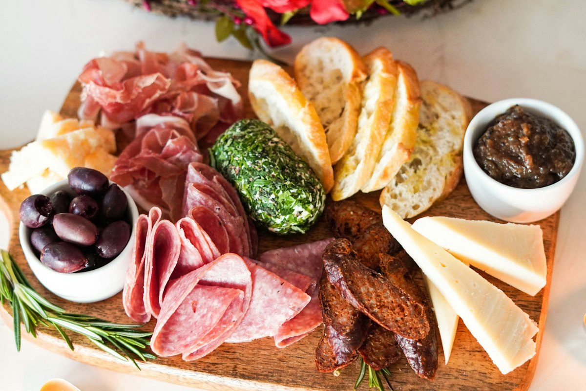 Sliced meat with vegetable and bread on brown wooden chopping board