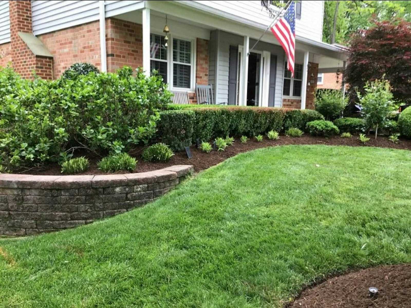 A front yard with a curved lawn, layered shrubs and a stone retaining wall