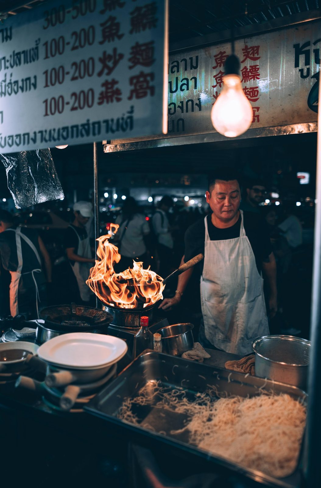 Cook working over a flaming grill at night