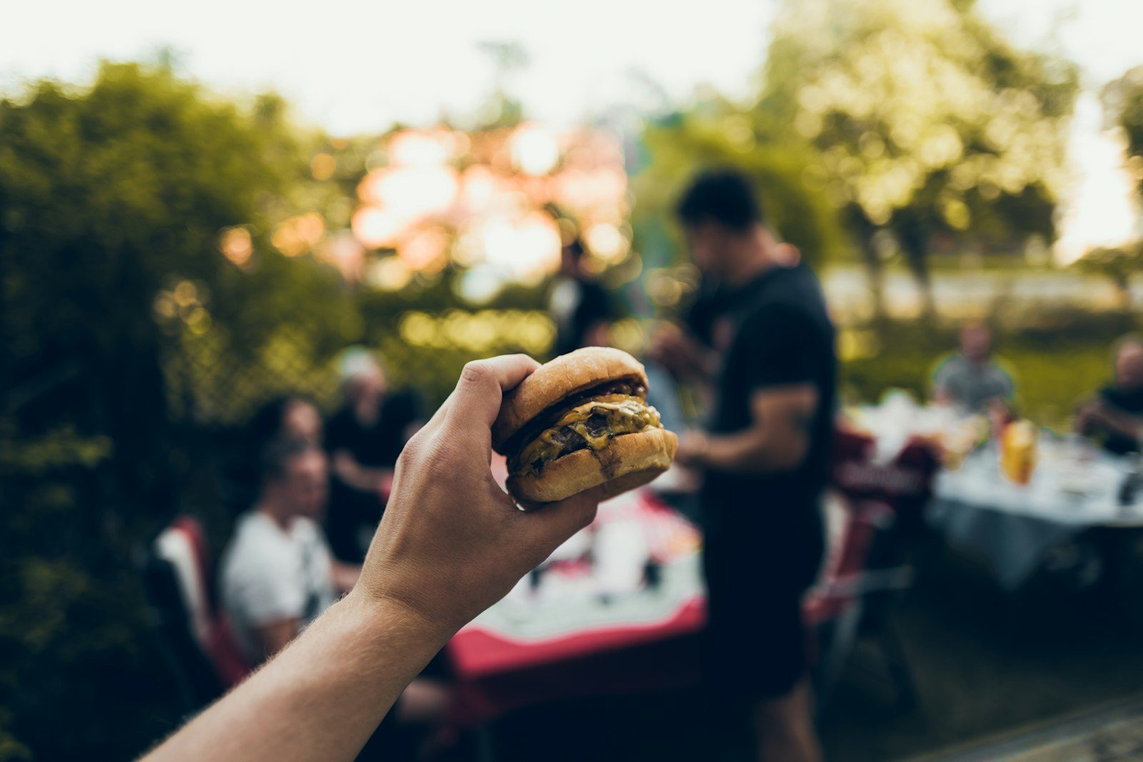 A hand holding a burger outdoors