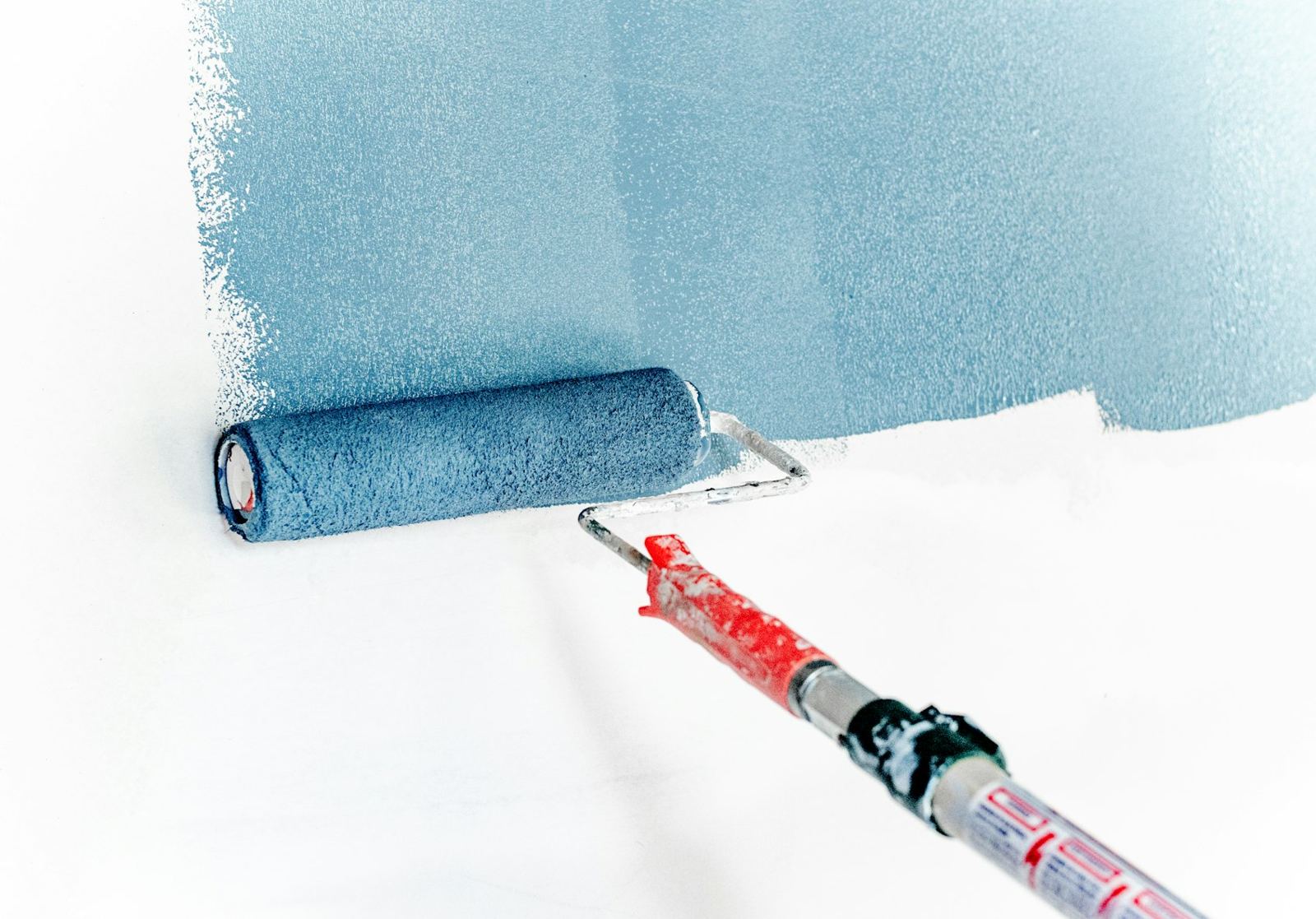 Paint roller applying soft blue paint to a white wall