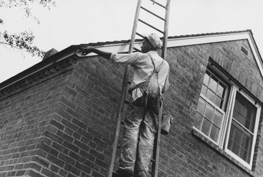 A painter working on a ladder against a brick building