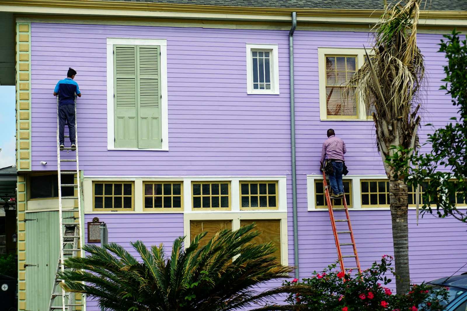 Two painters on ladders painting the siding of a house