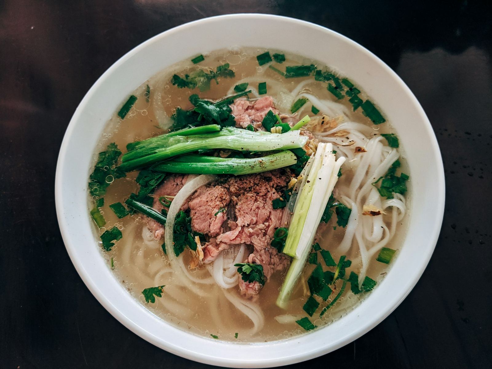 A bowl of beef phở with green onions and thin rice noodles