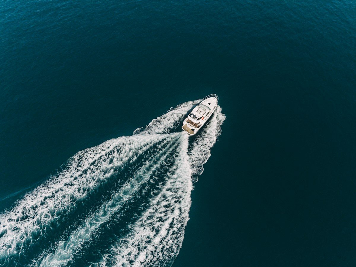A white motorboat moving through deep blue water, leaving a large white wake