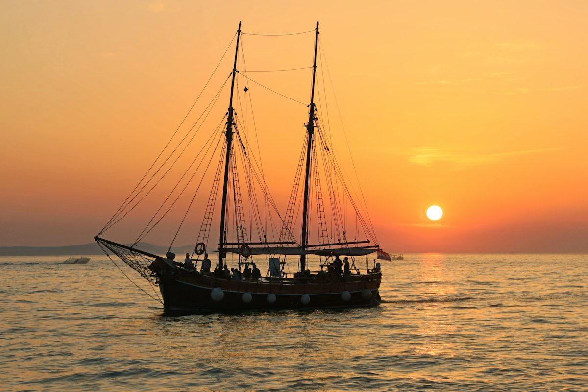 Black and white sailboat in body of water during sunset