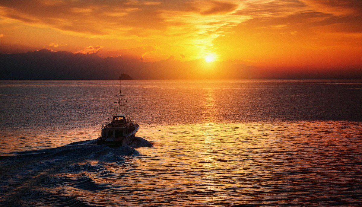 A boat traveling across a body of water at sunset