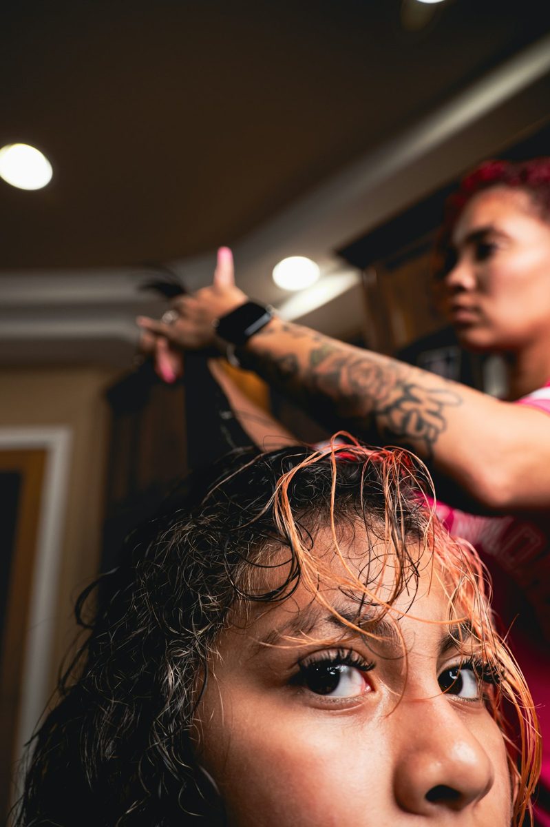 A person with tattooed arms styling the wet hair of another person