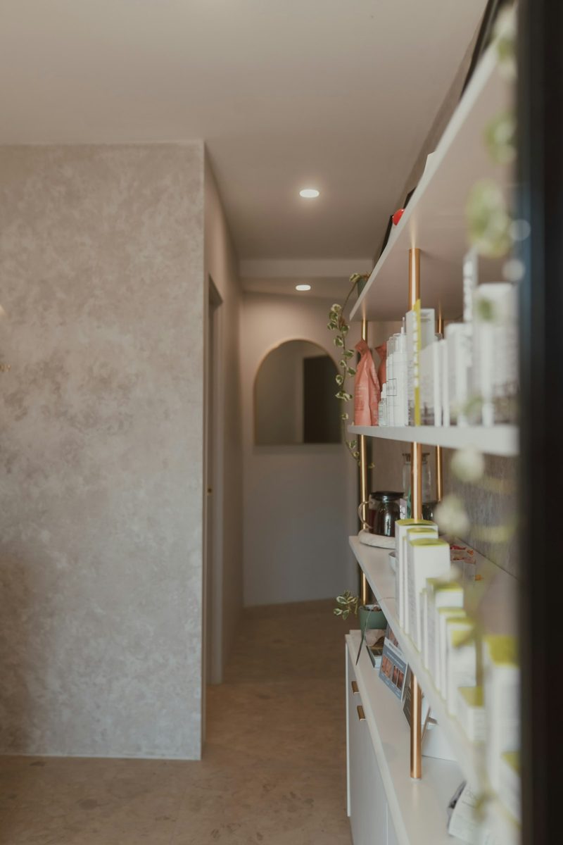 Shelves with skincare products in a bright hallway with a textured wall