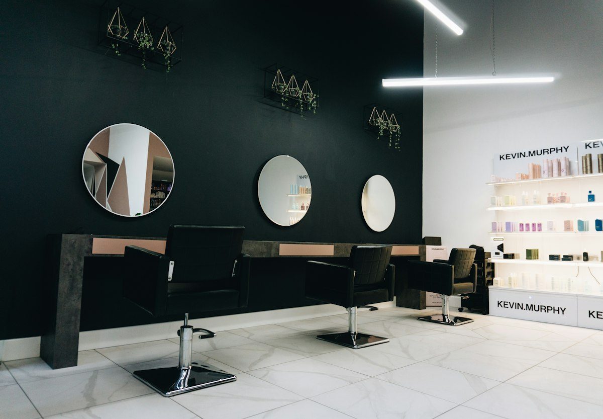 Three black salon chairs facing circular mirrors on a dark wall in a salon