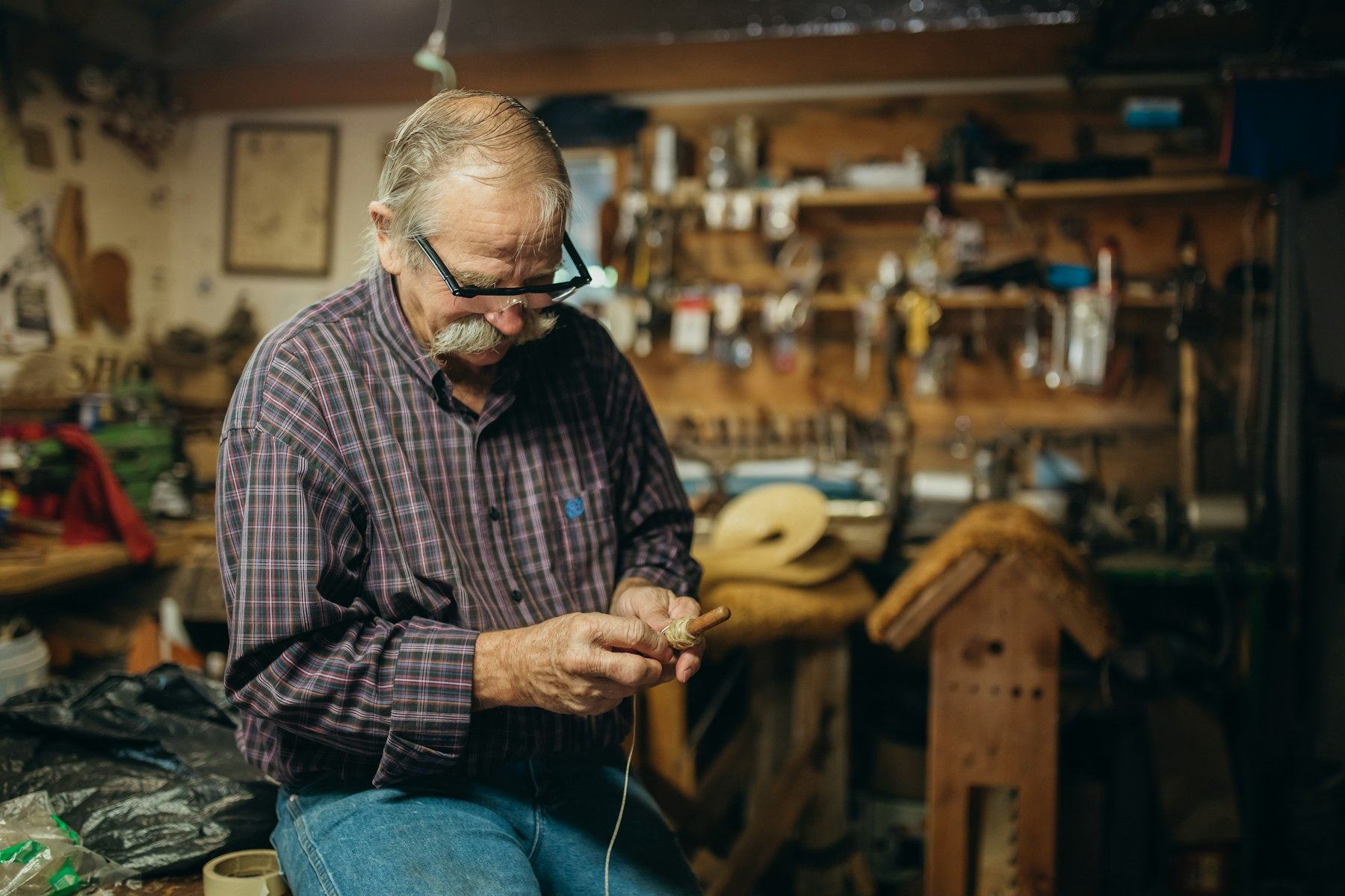 Man in black and white plaid dress shirt and blue denim jeans sitting on brown wooden