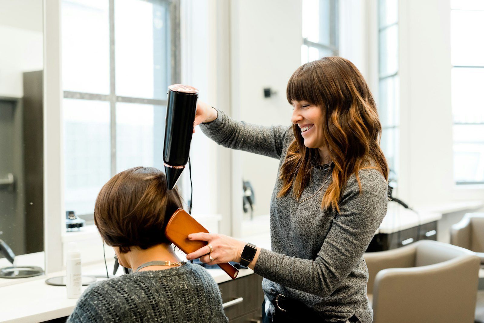 A stylist smiling while blow-drying a client's hair