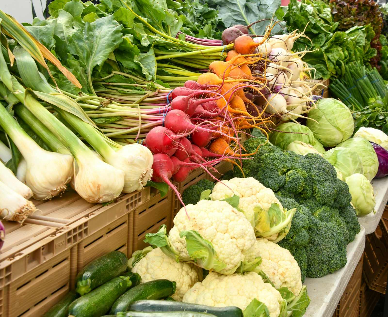 A market stall piled with leeks, radishes, cauliflower and greens