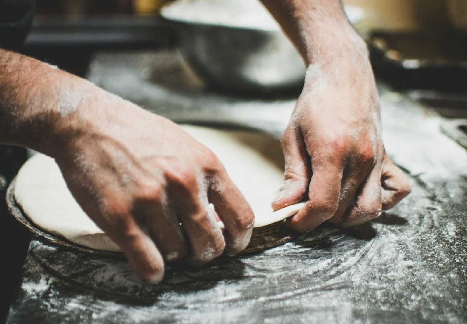 Hands stretching a round of pizza dough