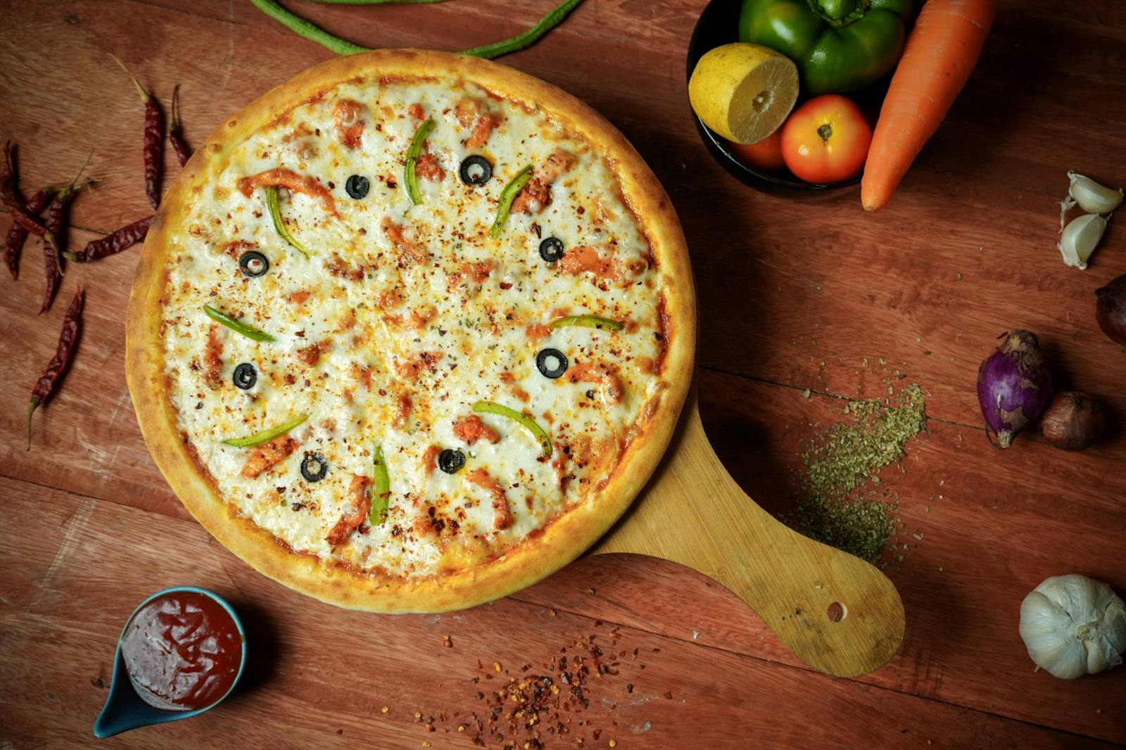 A loaded pizza on a wooden peel surrounded by ingredients