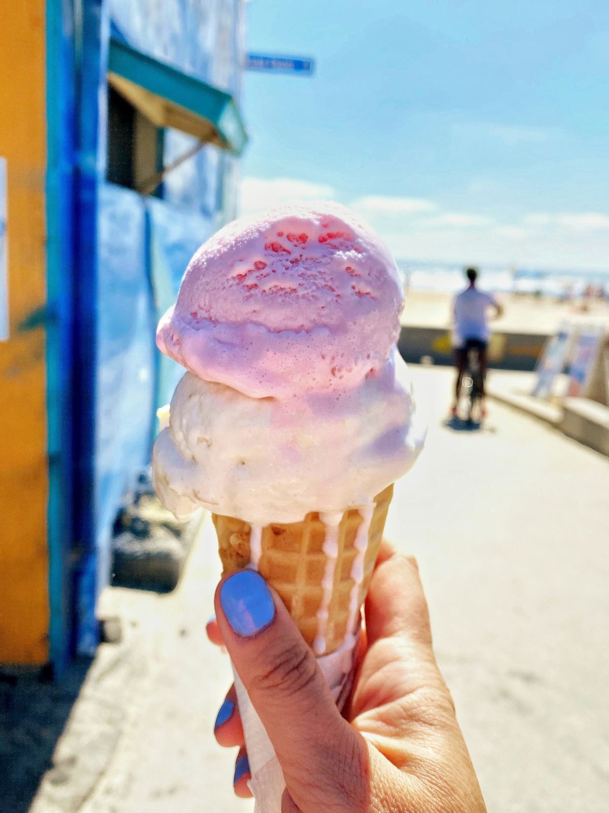 A pink double-scoop cone held up on a sunny boardwalk