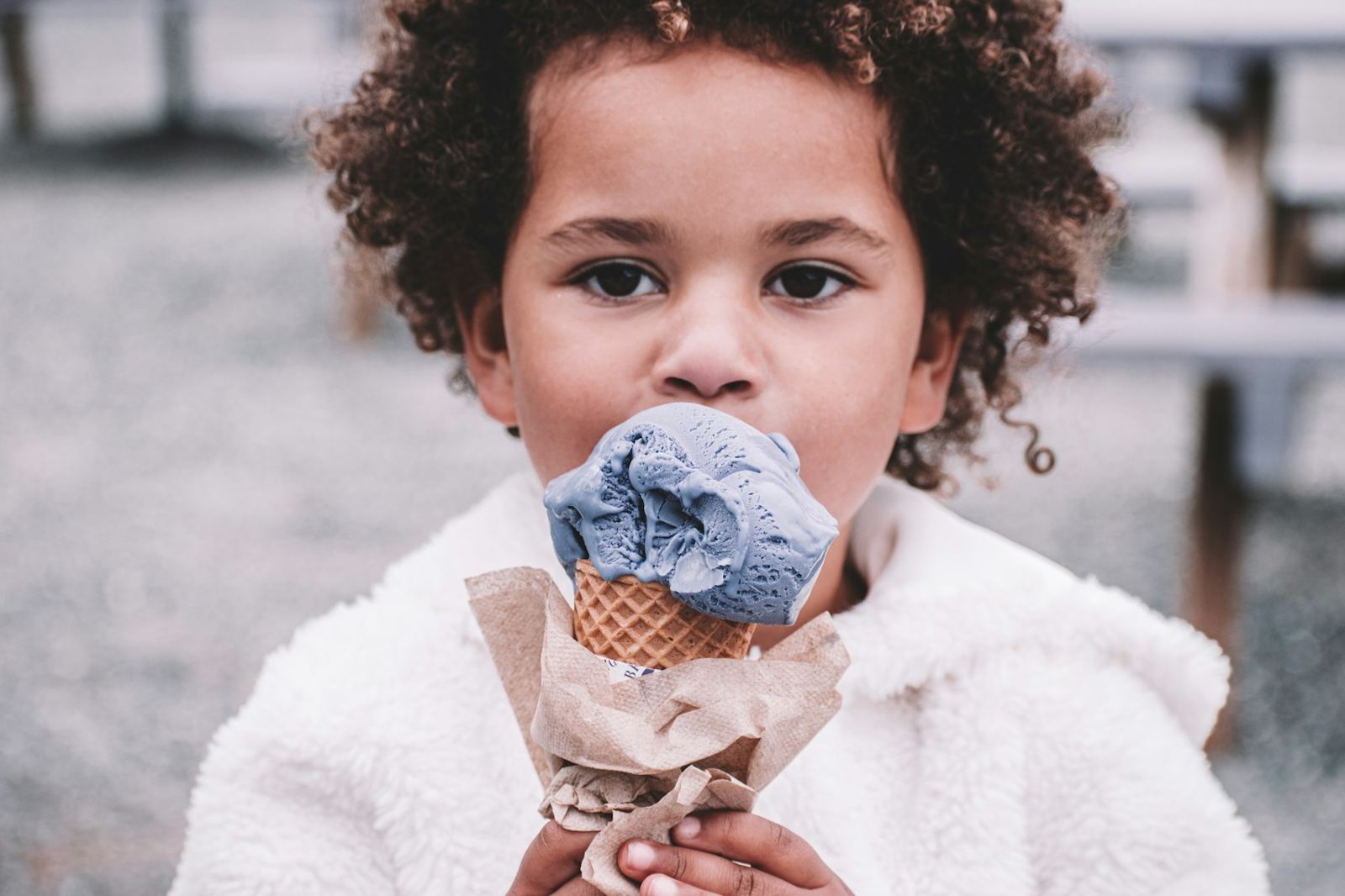 A child holding a blue scoop of ice cream in a cone