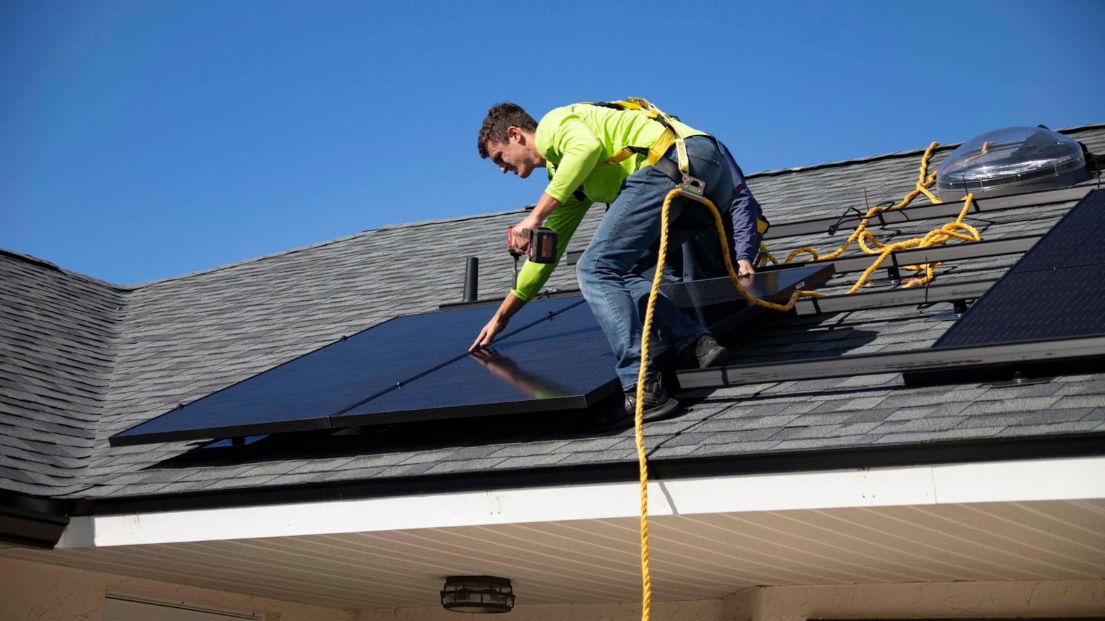 Installer in harness setting panels on a shingle roof